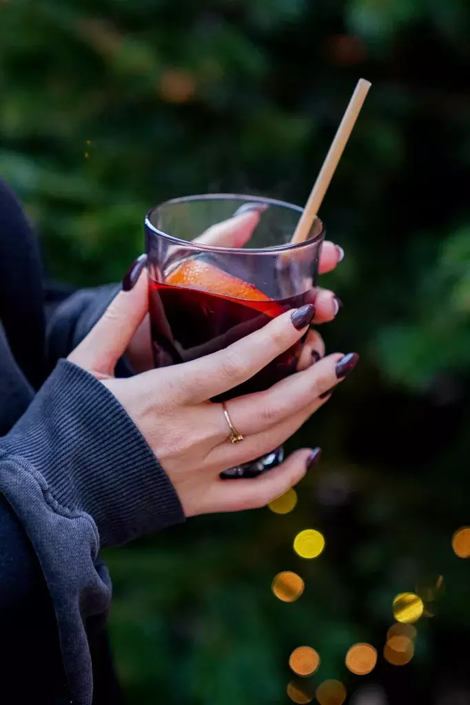 Verre de vin chaud tenu en main devant des lumières de Noël